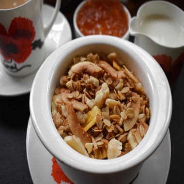 Bowl of Tropical Granola with tea cup, dish of marmalade and jug of milk in the background